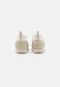 Light beige sneakers with a textured heel, grey accents, and a logo; features a pull tab for easy wear and a cushioned sole for comfort.