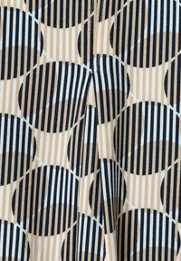 Textil mit einem geometrischen Muster aus großen schwarzen Ovale mit weißen und beigen Streifen. Der Stoff hat eine glatte Textur und verstärkte Nähte.