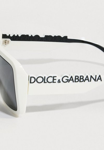 Λευκά υπερμεγέθη γυαλιά ηλίου με γκρι φακούς. Διαθέτουν το έντονο μαύρο λογότυπο "DOLCE & GABBANA" στο πλάι. Κατασκευασμένα από λείο πλαστικό υλικό.