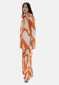Oranje en witte geprinte outfit bestaande uit een blouse met lange mouwen en brede broek, gemaakt van soepele stof met een vloeiende silhouet.