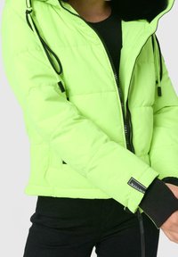 Giacca puffer verde neon con chiusura a zip, polsini elastici, tasche laterali e cappuccio con coulisse. Presenta dettagli neri e logo.