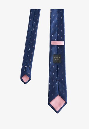 Tumesinine siidist lips, millel on väikesed roosad ja valged lillemustrid, näidates roosat voodrit ja "NEXT Occasion" brändisisalduse silt.