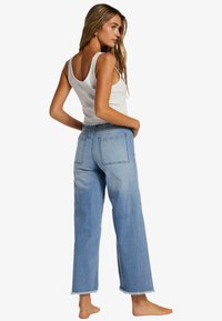 Light blue high-waisted wide-leg jeans with a frayed hem and two back pockets, paired with a white ribbed tank top.