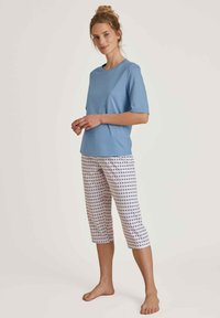Lichtblauw t-shirt met korte mouwen gecombineerd met witte capri-broeken met een klein blauw en rood geometrisch patroon. Katoenen materiaal, relaxte pasvorm.