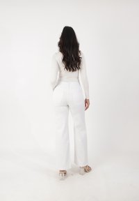 Jeans blancos de pierna ancha con cintura alta, textura de denim suave y dos bolsillos traseros. Combinados con sandalias de tacón cuadrado transparente.