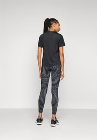 Sort atletisk t-shirt med korte ærmer, parret med mønstrede sorte leggings med geometriske designs. Fodtøj er sorte sneakers.