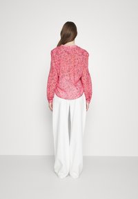 Blouse rose à motifs avec des manches longues, épaule ajustée et coupe décontractée, associée à un pantalon blanc ample. Texture lisse sur l'ensemble.