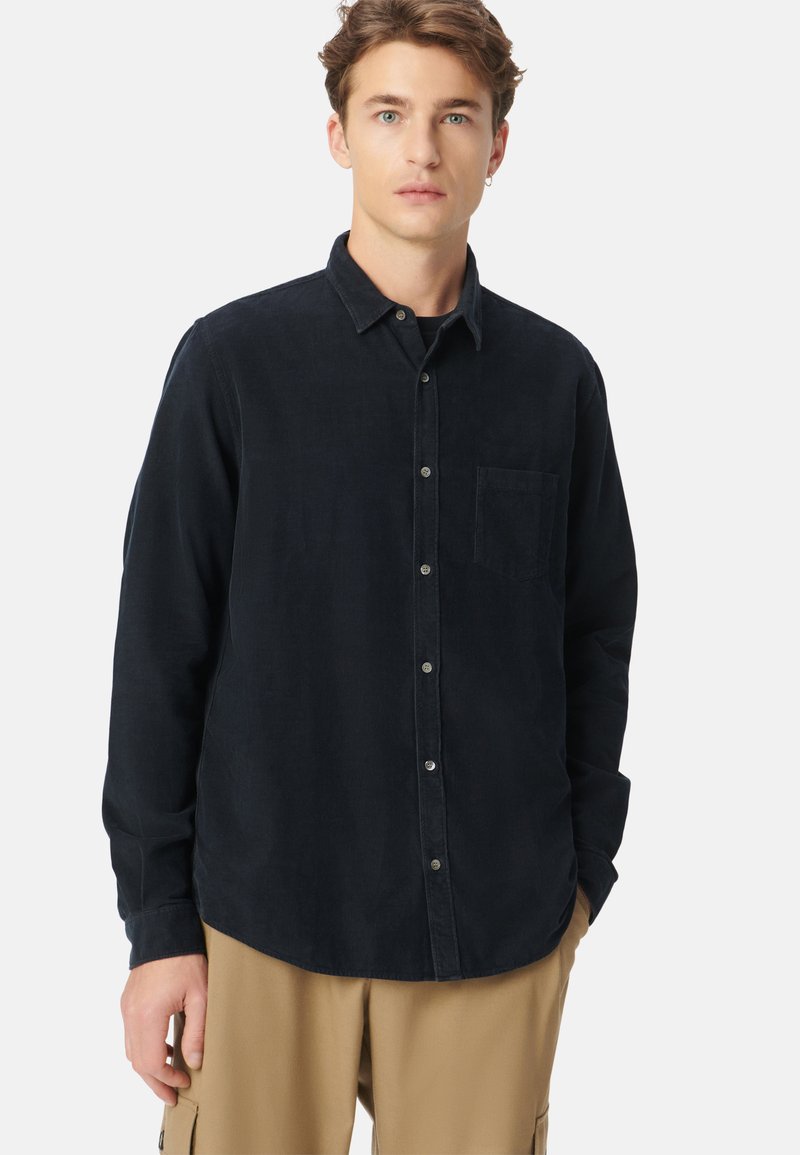 Camicia in corda blu navy con bottoni frontali, colletto a punta, taschino sul petto e maniche lunghe. Tela liscia e vestibilità rilassata.