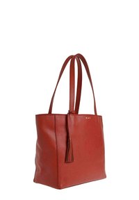 Sac fourre-tout en cuir rouge avec double sangle pour épaule et un détail à frange suspendu à une des sangles, présenté sur un fond blanc.