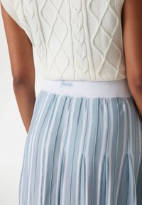 Gonna plissettata azzurro chiaro con strisce bianche e vita elastica, con il nome del marchio "Guess" ricamato in azzurro chiaro. Maglietta in maglia testurizzata.