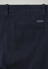 Marineblauwe trousers van gladde stof, met een achterzak en een klein merklabel. Eenvoudig ontwerp met subtiele stikseldetails.