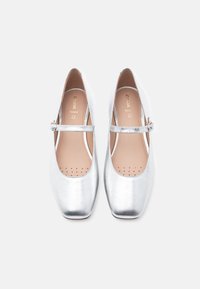 Ασημί μεταλλιζέ μπαλαρίνες με φάσα Mary Jane, στρογγυλεμένη μύτη και διάτρητη εσωτερική σόλα για αναπνευστικότητα. Ομαλή υφή και κομψός σχεδιασμός.