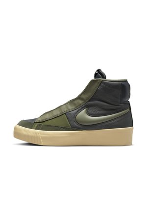 High-top sneaker met olijfgroene en zwarte leren bovenkant, beige rubberen zool en grote Nike-swoosh aan de zijkant.