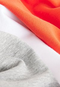 Trzy warstwy materiału: gładki szary, miękki biały i puszysty pomarańczowy, ukazujące różne tekstury i kolory w złożonym układzie.