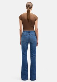 Niebieskie dzwony z podwyższonym stanem, wykonane z denimu; posiadają tylne kieszenie i czysty, minimalistyczny design. Brązowy dopasowany t-shirt.