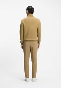 Beżowy sweter na drutach z wysokim kołnierzem, zestawiony z jasnobeżowymi spodniami i białymi trampkami. Gładka faktura, dopasowany krój i minimalne zdobienia.