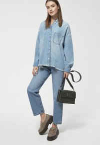 Jasnoniebieska, oversize koszula dżinsowa, dopasowane dżinsy, beżowe buty z czarną podeszwą oraz zielona torebka z logo. Szarpany detal u dołu.