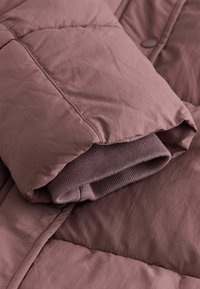 Îmbrăcăminte exterioară căptușită dintr-un material moale de culoare mauve, cu un design matlasat și o manșetă pliată cu textură de tip rib. Luciu ușor, suprafață netedă.