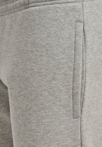Lichtgrijze sweatpants gemaakt van zachte stof, met een zijzak met subtiele stiksels, een gladde textuur en een elastische tailleband.