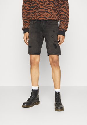 Black denim shorts with distressed details, paired with black lace-up boots and white crew socks. Model wears a brown patterned sweater.