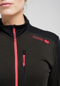 Sort og mørk olivengrønn zip-up jakke med høj krave, med røde lynlåsdetaljer og logo. Struktureret stof med lynlåslomme på brystet.