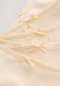 Jasnobeżowa tkanina z koronkową lamówką i małymi satynowymi kokardkami, charakteryzująca się gładką fakturą oraz klasycznym, delikatnym wzorem.