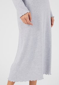 Abito grigio a costine con maniche lunghe, polsini ondulati e orlo fluente. La texture morbida e il design aderente enfatizzano il comfort e la facilità di utilizzo.