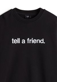 Sweat-shirt noir à col rond avec le texte blanc « tell a friend. » centré sur la poitrine, et une étiquette de la marque Vans à l'intérieur du col.