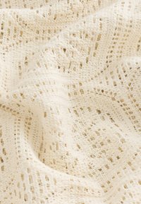 Jasnokremowa tkanina z wzorem o otwartej strukturze i teksturowanej powierzchni, prezentująca miękki, przewiewny wygląd.