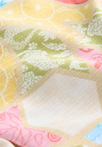 Veelkleurige stof met bloem- en geometrische patronen in geel, groen, roze en blauw. Satijnachtige textuur met een gladde afwerking.