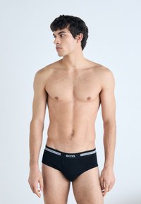 Zwarte boxershort met elastische tailleband, voorzien van grijze strepen en het "BOSS"-logo. Gladde stof met een aansluitende pasvorm.