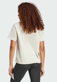 Kurzärmliges, crèmefarbenes T-Shirt aus Baumwolle mit lockerem Schnitt und glatter Textur, kombiniert mit schwarzen Leggings.