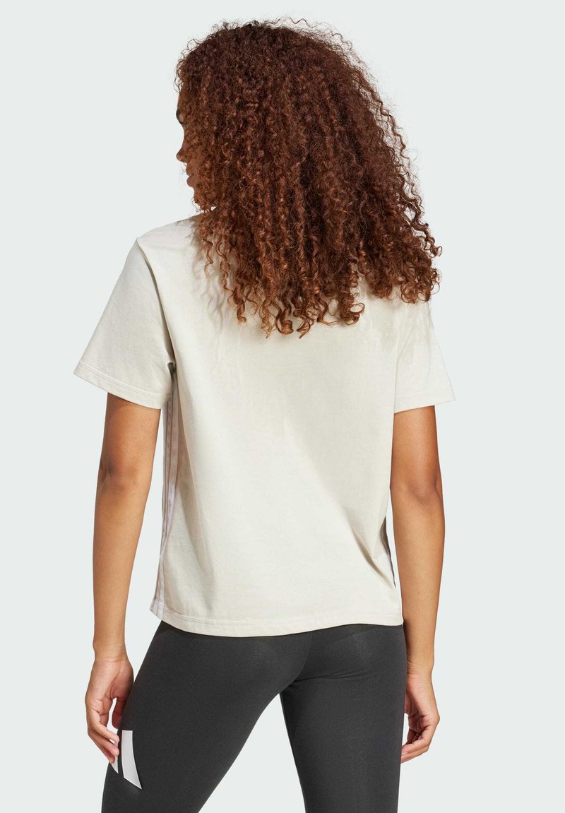 Kurzärmliges, crèmefarbenes T-Shirt aus Baumwolle mit lockerem Schnitt und glatter Textur, kombiniert mit schwarzen Leggings.