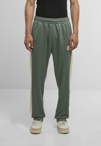 Grüne Sporthose mit elastischem Bund, seitlichen cremefarbenen Streifen und Logodetail. Hergestellt aus glattem, leichtem Material.