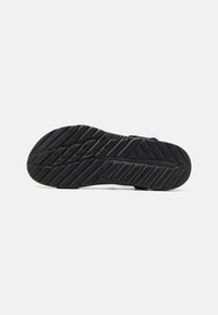 Black athletic shoe sole with textured grip patterns, multiple grooves, and a rounded heel. Material appears rubberized and durable.