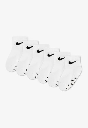 Seks par hvide ankelstrømper med sorte Nike swoosh-logoer på manchetterne og tæerne, arrangeret i en let buet linje på en hvid baggrund.