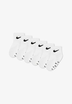 Seks par hvide ankelstrømper med sorte Nike swoosh-logoer på manchetterne og tæerne, arrangeret i en let buet linje på en hvid baggrund.