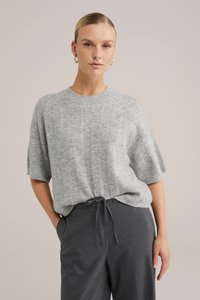 Pelēks adīts puloveris ar ribainu struktūru un īsām piedurknēm, kopā ar tumšām svītrainām biksēm. Iespējo apaļu kakla izgriezumu un brīvu piegriezumu.