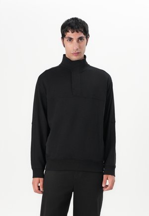 Black pullover sweatshirt with a high collar, featuring a front seam detail and long sleeves, made of soft, smooth fabric.