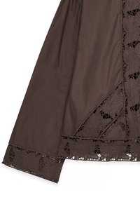 Tessuto marrone con bordo in pizzo floreale e dettagli intagliati. Presenta un orlo dritto e una superficie texturizzata. Progettato con un aspetto a strati.