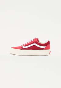 Red canvas sneakers with white accents, flat laces, padded collar, and a thick cream rubber sole. Side features a signature wave design.