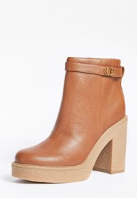 Hnědé kožené kotníkové boty s texturovaným povrchem, blokovým podpatkem a zlatým logem na boku. Platforma pro zvýšení výšky.