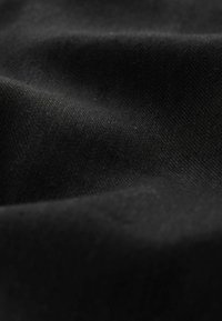 Schwarzer Stoff mit glatter Textur und leichtem Glanz, der subtile Falten und Knicke zeigt, die seine Weichheit und Tiefe betonen.