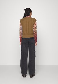 Cable-knit, sleeveless sweater in olive green with a ribbed hem, paired with oversized dark gray cargo pants featuring side pockets.