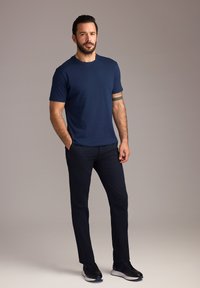 Granatowa koszulka z krótkim rękawem i okrągłym dekoltem oraz ciemne spodnie. Stylizację uzupełniają granatowe buty.