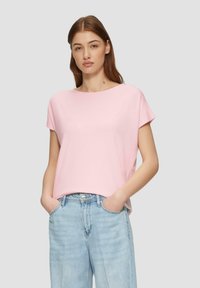 Rosa Kurzarm-T-Shirt mit rundem Halsauschnitt. Aus weichem Material gefertigt und mit einer legeren Passform. Kombiniert mit hellblauen, lockeren Jeans.