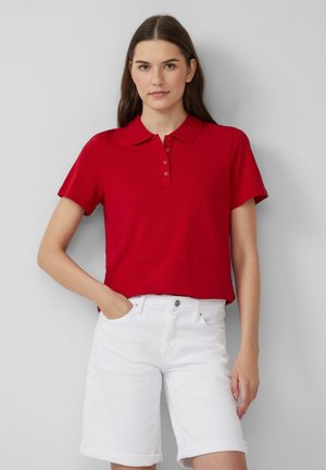 Polo rouge à manches courtes avec un col et une patte de boutonnage à trois boutons, associé à un short en denim blanc à revers.