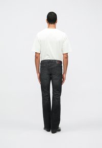 Melni džinsa bikses ar taisnu bikšu kāju siluetu, kopā ar vienkāršu baltu T-kreklu. Redzamas aizmugurējās kabatas ar krāsainu akcenta tagu.