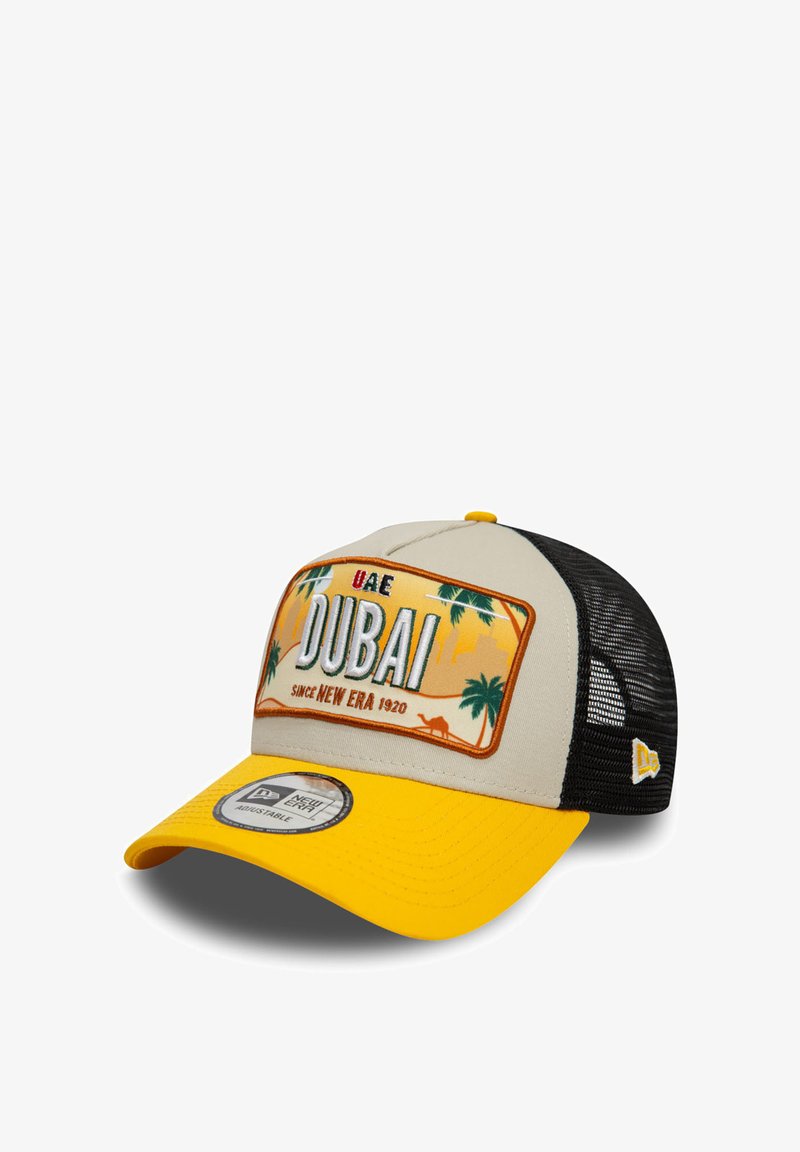 Gorra de béisbol con un panel frontal beige, visera amarilla y parte trasera de malla negra. Parche decorativo con gráficos de "Dubái" y palmeras.