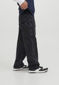 Svarta denim cargo byxor med flera fickor, en lös passform och en något blekt textur, tillsammans med svartvita sneakers.